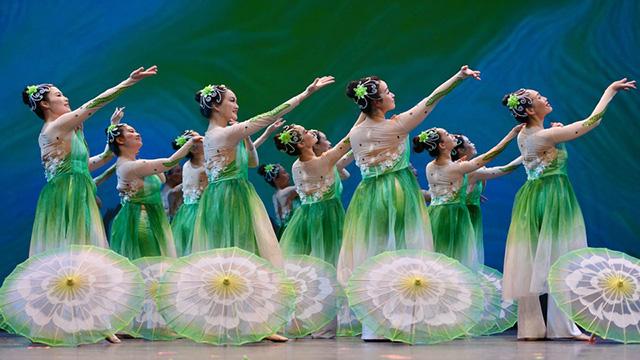 a group of dancers all turning to the left stand with an arm upraised and an open umbrella on the floor next to them