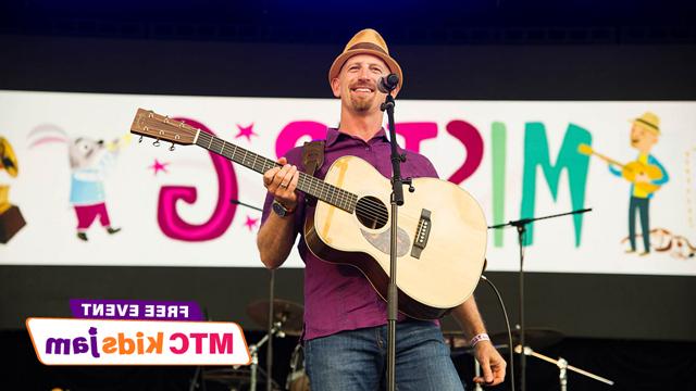 Ben Gundersheimer on stage with a guitar and a banner behind him that reads Mister G